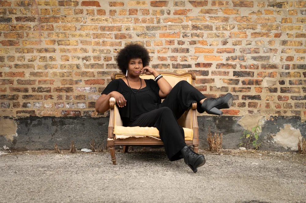 Jeanette Thomas seated in an old armchair in front of a brick wall